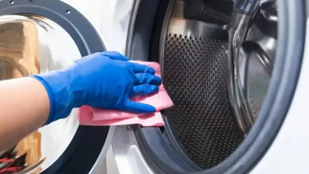 Persona limpiando la goma de la puerta de una lavadora con un paño